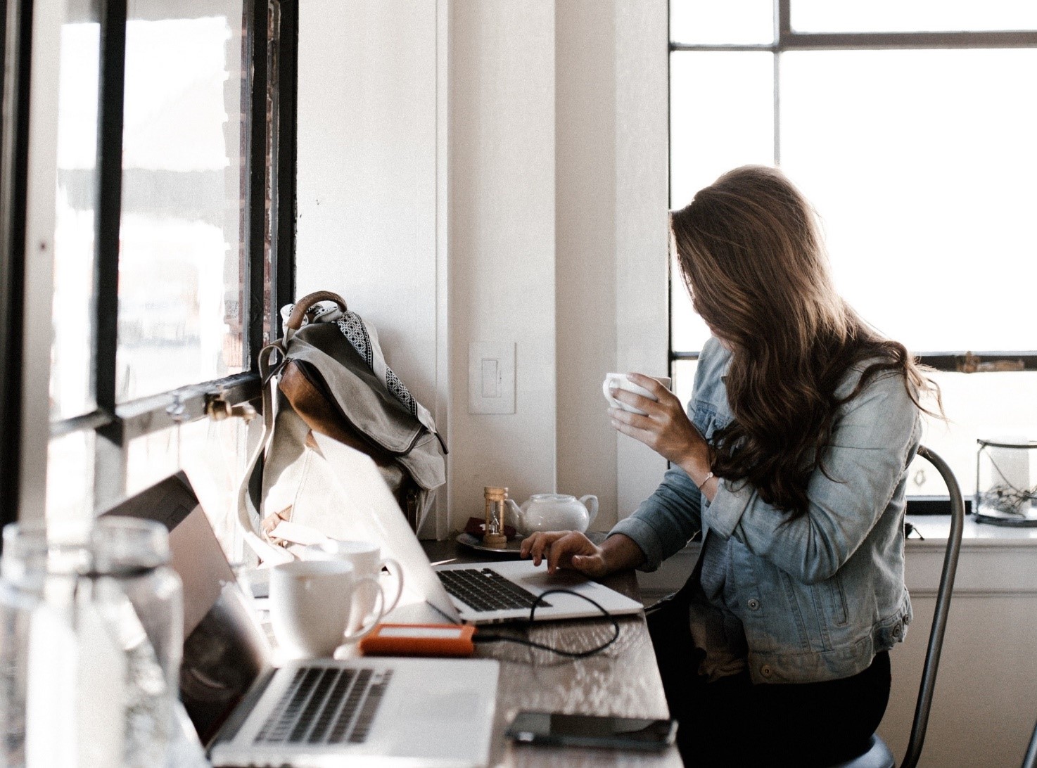 A young girl holding a cup of coffee while being on the computer